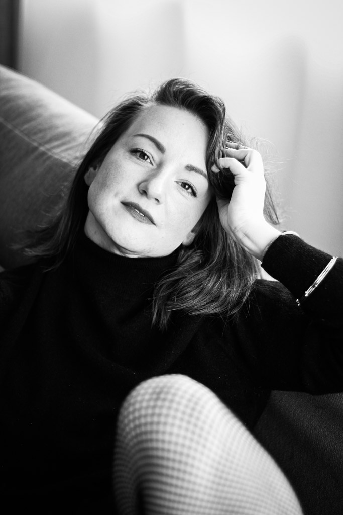 Närbild i svartvitt av Maggys händer mot tyg med subtila skuggor och kornig struktur.